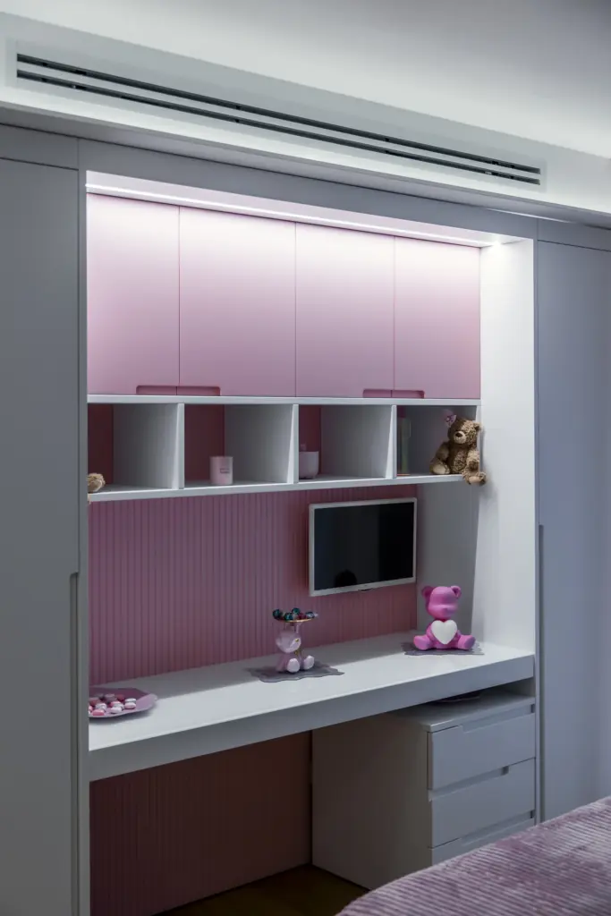 Zona studio moderna integrata in una camera da ragazza, con mobili bianchi e rosa, scrivania, scaffali e decorazioni a tema.