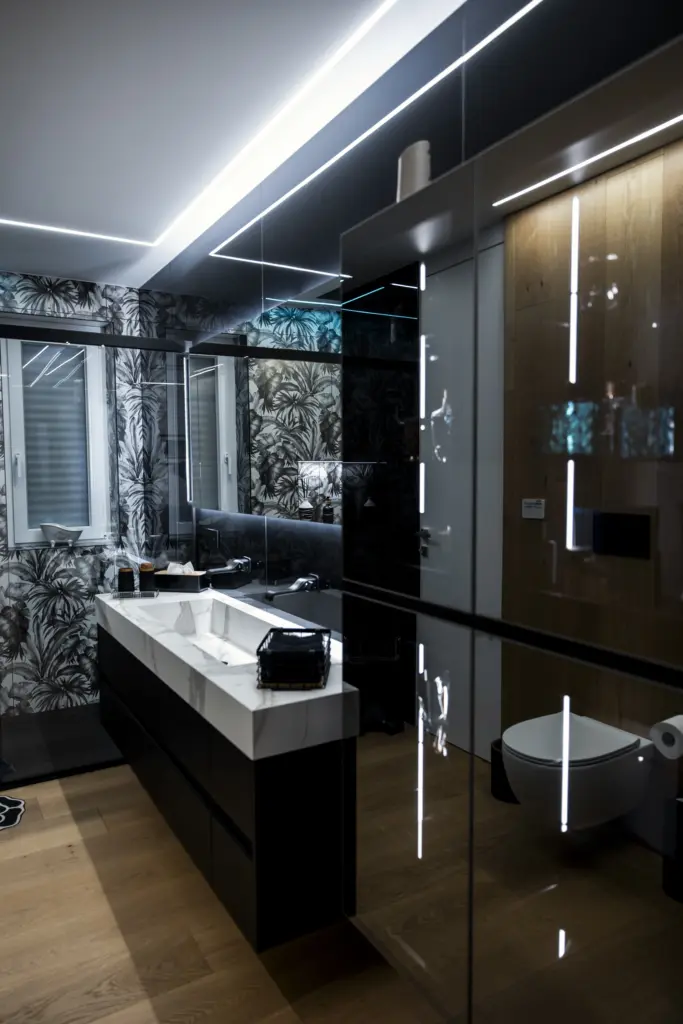 Bagno di design con lavabo in marmo, pareti con carta da parati a tema tropicale, specchio retroilluminato e dettagli in legno.