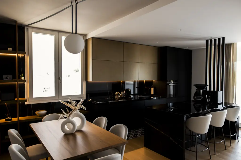 Cucina contemporanea con mobili neri opachi, pensili bronzati, isola centrale in marmo nero e tavolo in legno massello con sedute imbottite.