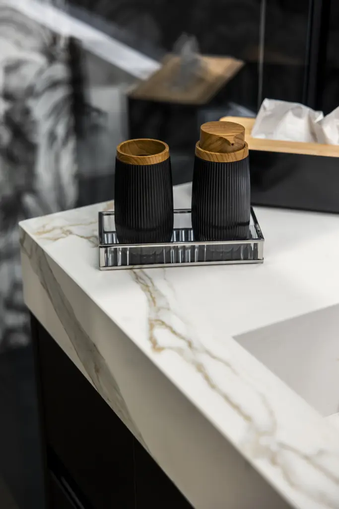 Dettaglio di un bagno elegante con lavabo in marmo bianco venato e accessori neri con finiture in legno.